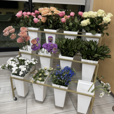 12 small white containers of different colored flowers in a gold stand.