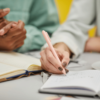 Hands of two people, one is writing the other is clasped together.